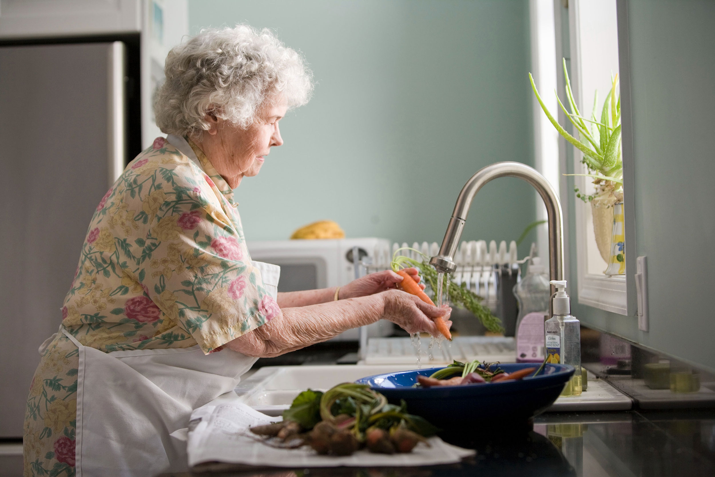 older woman washing vegetables in a kitchen