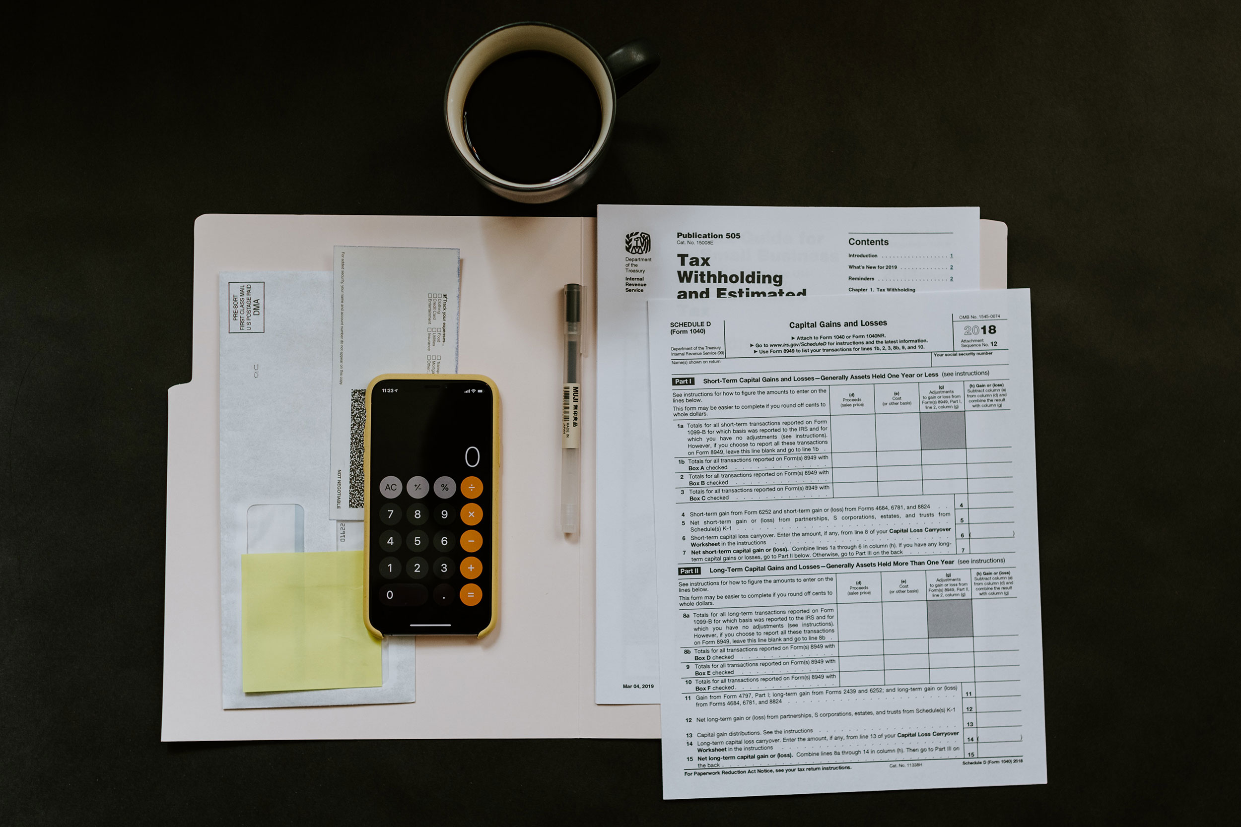 desk with a mug and a calculator sitting on an open folder revealing tax forms